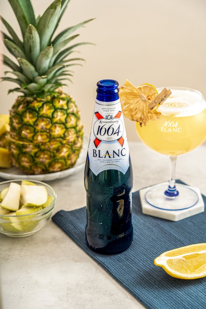 1664 Blanc bottle beside a citrus cocktail and fresh pineapple