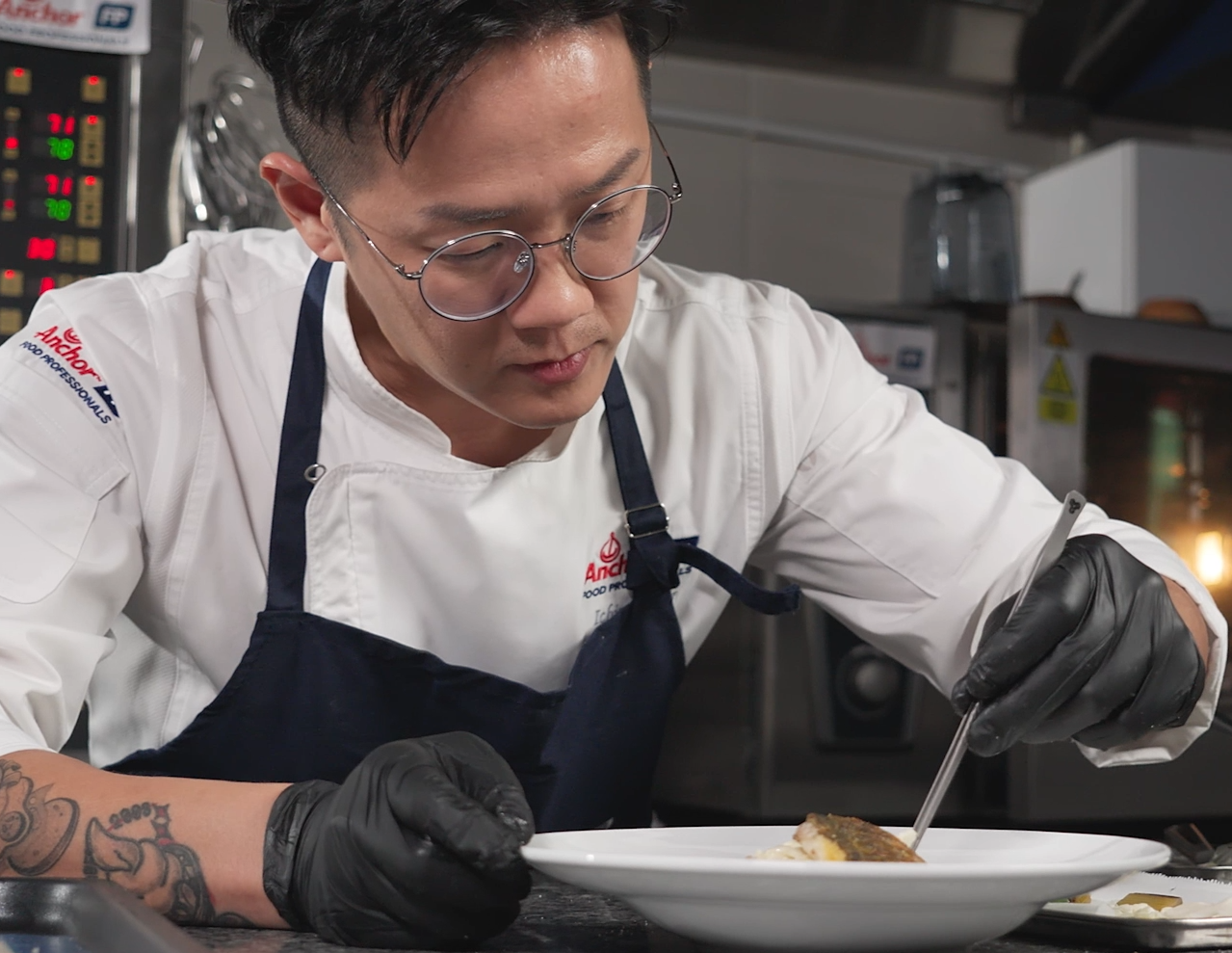 Chef in whites plating a dish in a professional kitchen