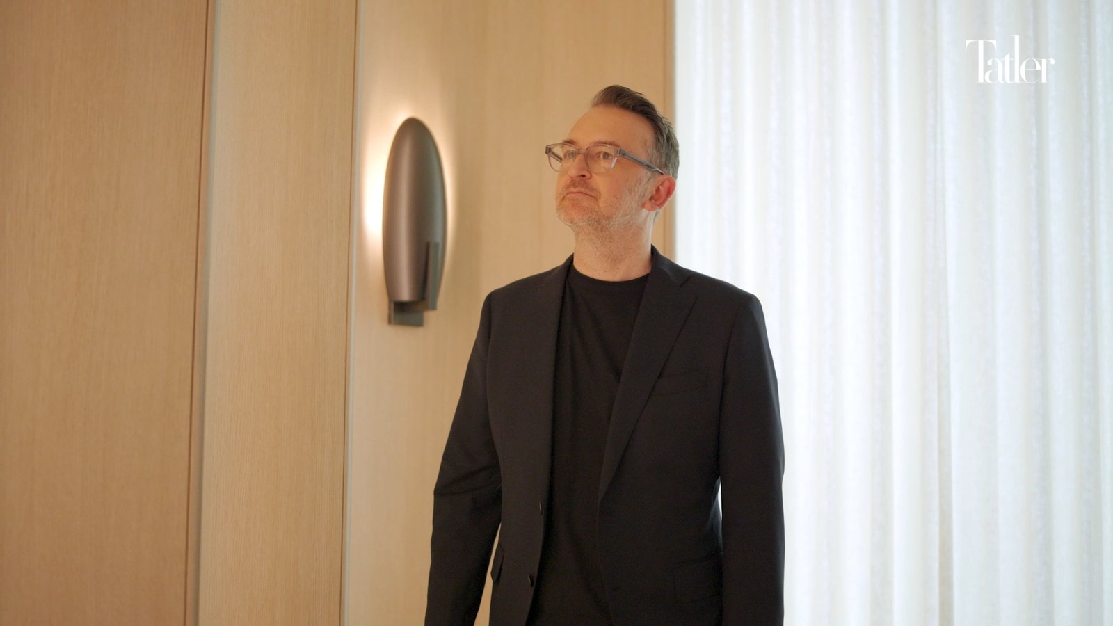 Portrait subject in a dark suit against a soft curtained interior